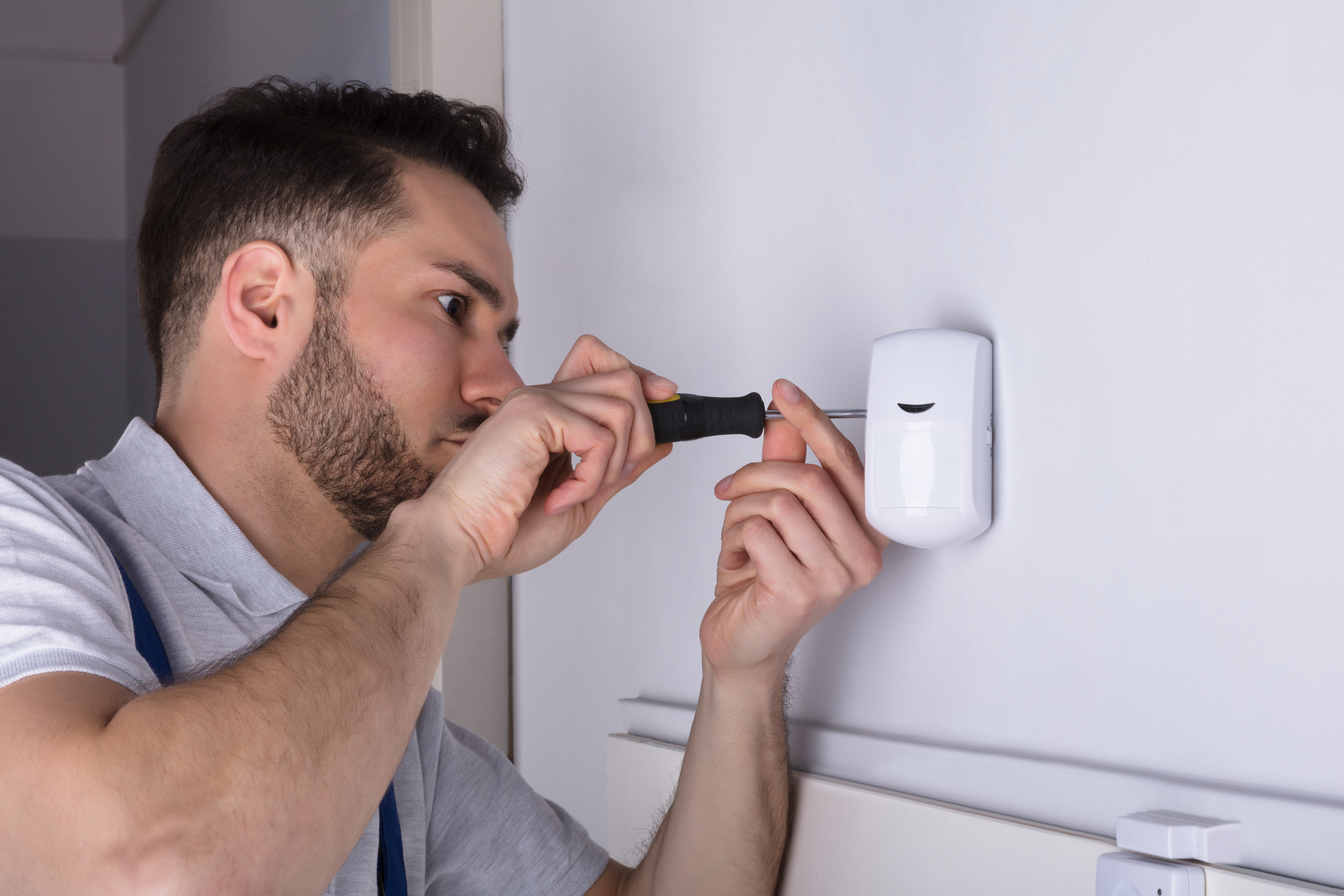 Close-up Of A Young Male Electrician Installing Security System Door Sensor On Wall