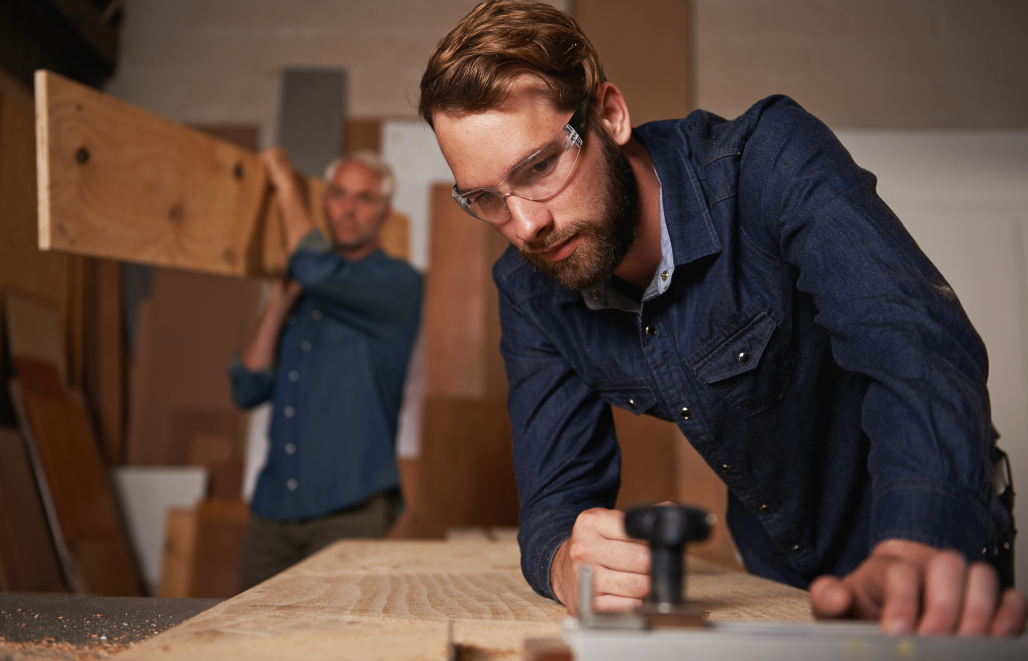 Carpentry collaboration, carpenter and men work in workshop on design project with vocation and creative skill. Teamwork, male worker cutting wood with power tools and father and son working together.