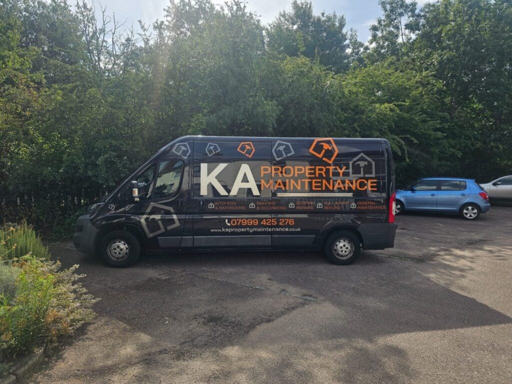 Black KA Property Maintenance van with orange and white branding parked beside trees.